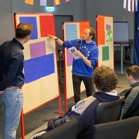 Vortragende stehen an einer Pinnwand vor Auszubildenden 